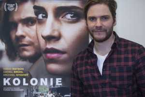 Před plakátem k filmu Kolonie, kde hrál po boku Emy Watson.