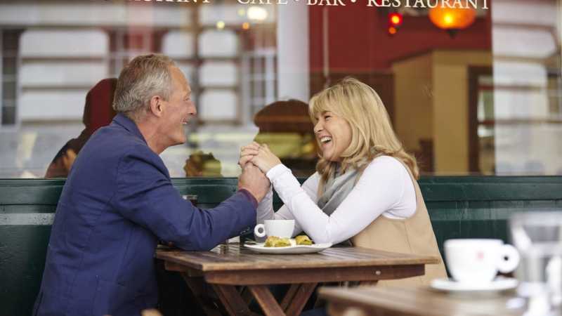 Mature dating couple holding hands at sidewalk cafe table